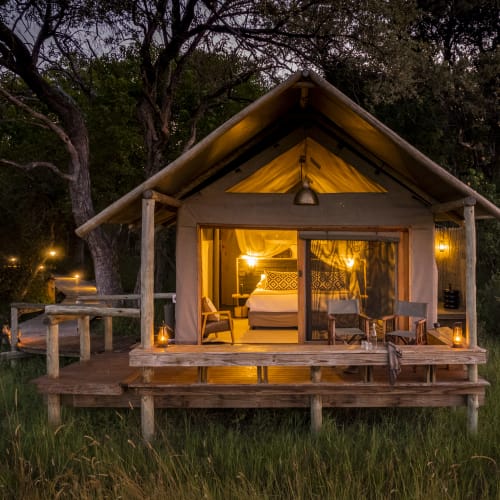 A cozy bedroom inside a wooden cabin with warm lighting, located on a deck in a forested area.