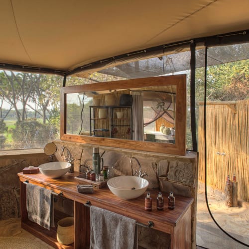 Open-air bathroom in a rustic, tent-like structure with stone and wood elements, surrounded by natural scenery.