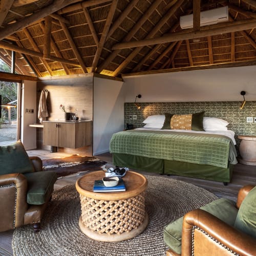 Luxurious bedroom with a king-size bed, green bedding, and rustic wooden interior with high vaulted ceiling.