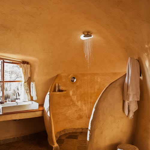 Ein gemütliches Badezimmer mit warmen, gebogenen Wänden, einem kleinen Fenster mit Vorhängen und einer begehbaren Dusche mit Regendusche.