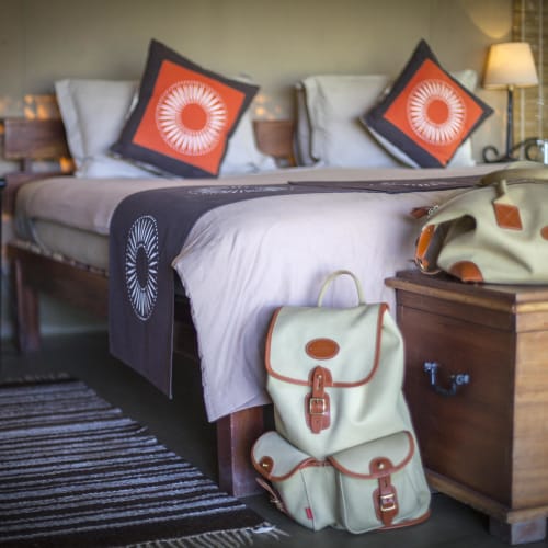 A cozy guest bedroom with a bed, two lantern-style lamps, and travel bags on a wooden chest at the foot of the bed.