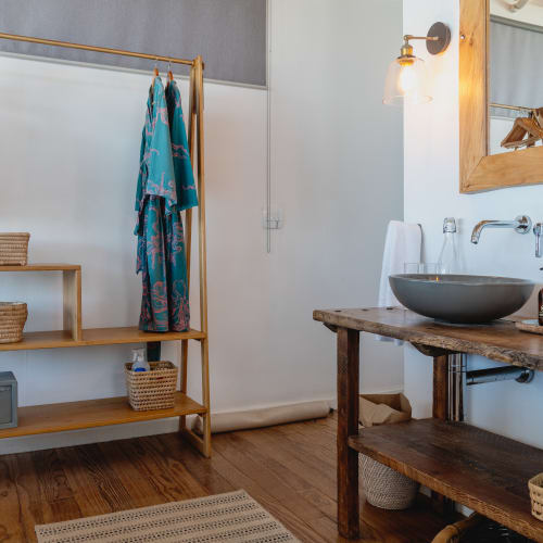 Ein Badezimmer mit zwei Waschtischen, einem Holzregal mit Körben und Kleidung, und einem großen Wandspiegel.