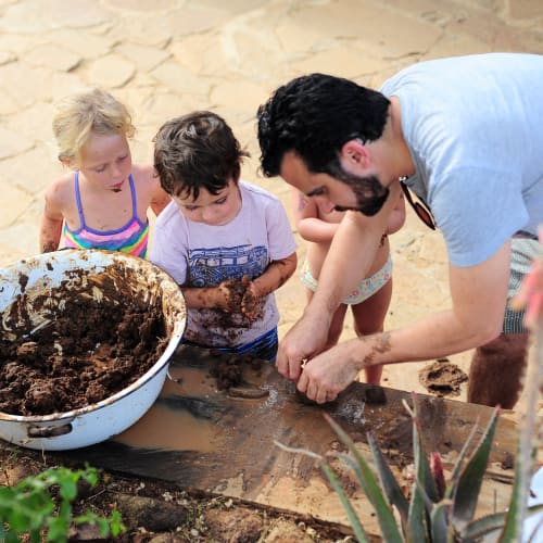 A man demonstrating planting activities to three children outdoors, with soil and plants on a wooden surface.