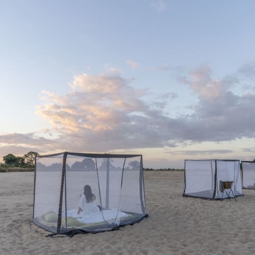 Ein Mädchen schläft in einem Campingzelt am Strand bei Sonnenuntergang, mit drei weiteren Zelten in der Nähe.