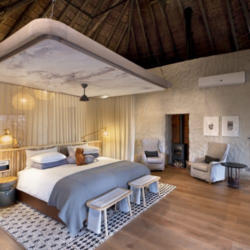 Luxurious bedroom inside a thatched-roof house with a king-size bed, sitting area, and modern decor in South Africa.