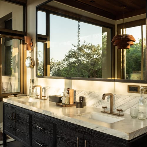 Luxuriöses Badezimmer mit Doppelwaschbecken, Marmor-Arbeitsplatte und großen Fenstern mit Blick auf das Grün draußen.