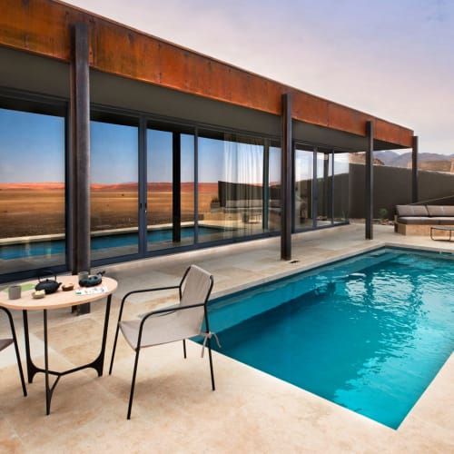A modern outdoor patio with a small pool, overlooking a desert landscape with mountains in the distance.