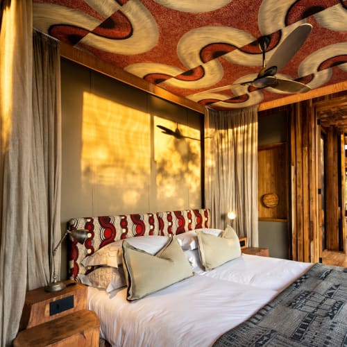 Luxuriöses Schlafzimmer mit verziertem Decke, großem Bett und Vorhängen, mit warmem Licht und Holzakzenten in einer Safari-Lodge.