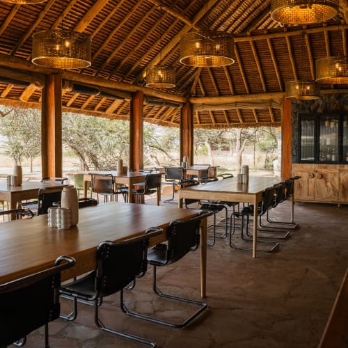 Inside a rustic, open-air dining area with wooden furniture and a view of nature outside.