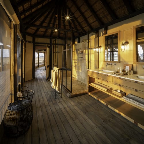 Luxuriöses Badezimmer mit Doppelwaschbecken, großen Spiegeln und warmem Licht in einer geräumigen Suite mit Blick auf eine Außenterrasse.