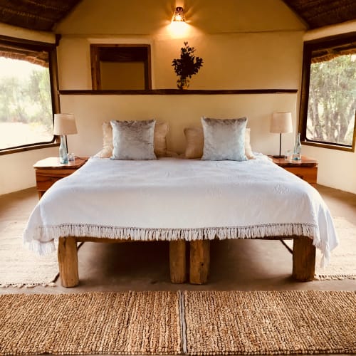 A cozy bedroom with a large double bed, two nightstands with lamps, and large windows with views of greenery.
