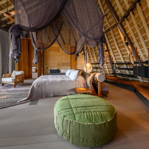 Ein gemütliches Schlafzimmer mit einem Bett, einem grünen Hocker und einem Baldachinnetz in einer stilvollen Lagerhütte in Botswana.