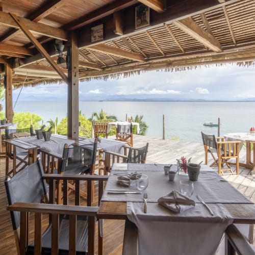 Eine abgelegene Restaurantterrasse mit Holzmöbeln und Blick auf den Ozean und Boote.