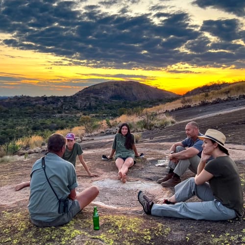 Eine Gruppe von fünf Personen sitzt auf dem Boden und unterhält sich bei Sonnenuntergang in den Matobo Hills.