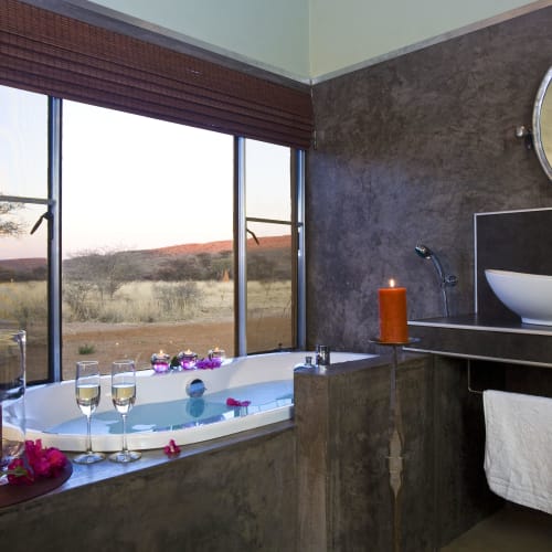 Ein luxuriöses Badezimmer mit einer großen Badewanne neben einem Fenster mit Blick auf eine natürliche Landschaft, dekoriert mit Kerzen und Blumenblättern.