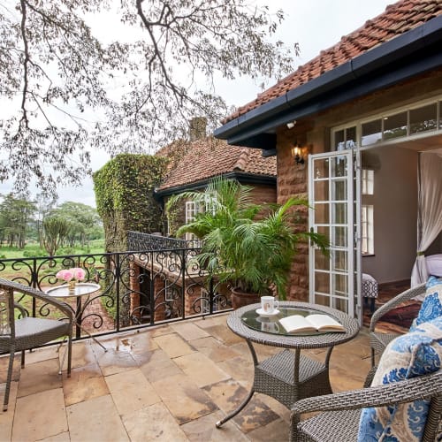 Charming outdoor terrace of a suite at Giraffe Manor in Kenya, with wicker chairs, a small table, and lush greenery in the background.