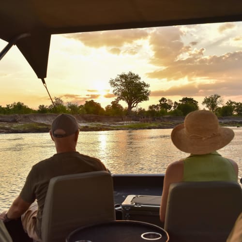 Menschen sitzen in einem Boot und genießen den Blick auf einen Fluss bei Sonnenuntergang in Simbabwe.