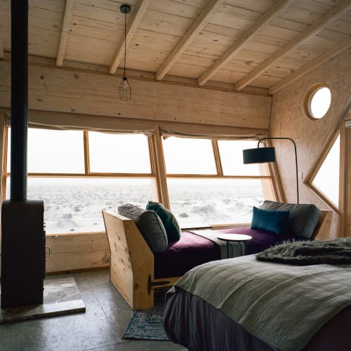Cozy bedroom with large windows overlooking a snowy landscape, furnished with a bed, a sofa, and a floor lamp.