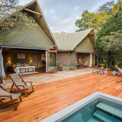 Luxus-Zelt mit Veranda und Holzveranda, blickt auf einen üppigen grünen Wald mitOUTDOOR-LEGENDE-OUTDOOR-Sesseln und einem Hot Tub.