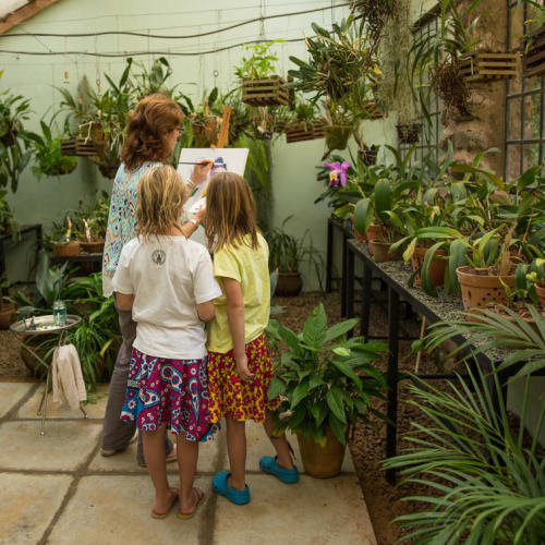 A woman and three children observing plants and artwork in a lush greenhouse filled with potted plants.
