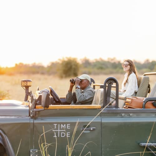 Ein Paar in einem Safari-Fahrzeug beobachtet während eines Sonnenuntergangs eine grasige Ebene.