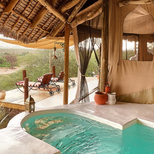 Luxurious tent suite with a private pool overlooking a savannah landscape, featuring wooden and canvas structures.