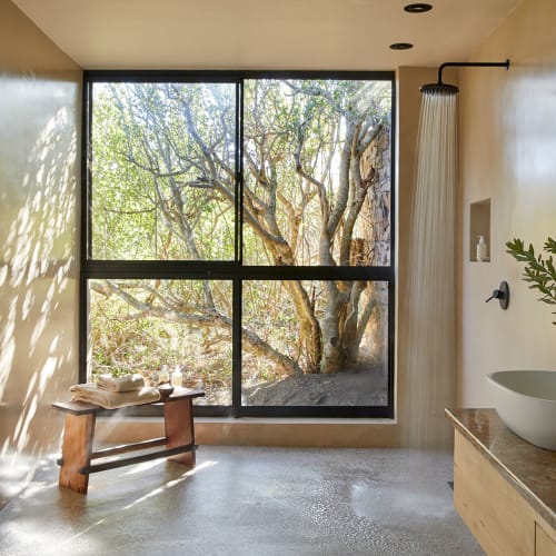 Spacious bathroom featuring a large window with a view of trees, a wooden bench, a basin sink, and a shower with a curtain.