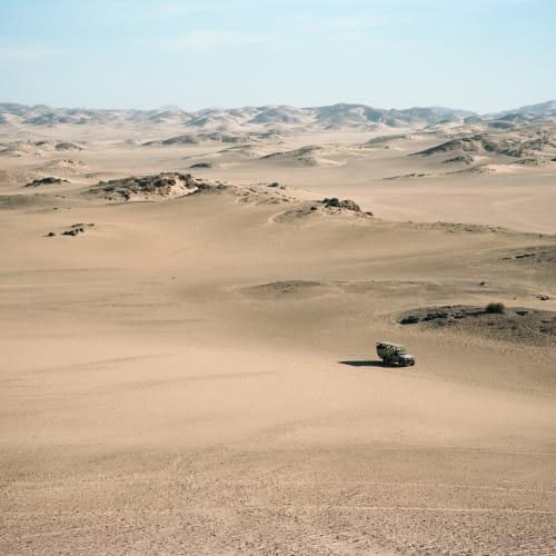 A vehicle driving through sand dunes in a desert landscape during a game drive in Namibia.