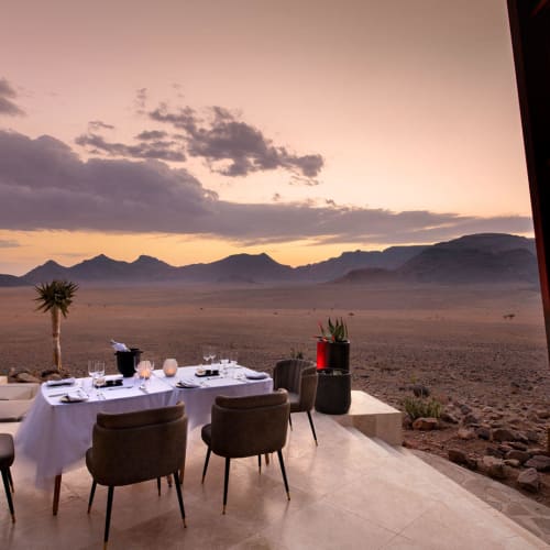 Elegant outdoor dining setup on a terrace overlooking a desert landscape at sunset.