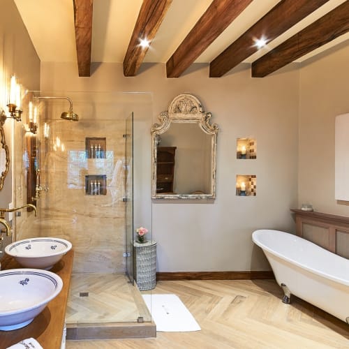 Luxury bathroom featuring two ornate mirrors, a vintage bathtub, and wooden ceiling beams.