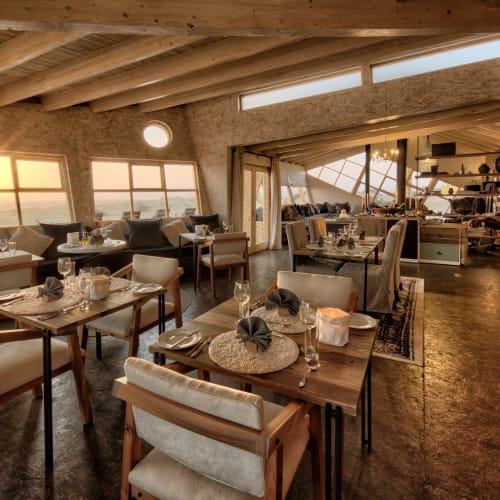 Elegant dining area inside a lodge with large windows showing a sunset over the Skeleton Coast in Namibia