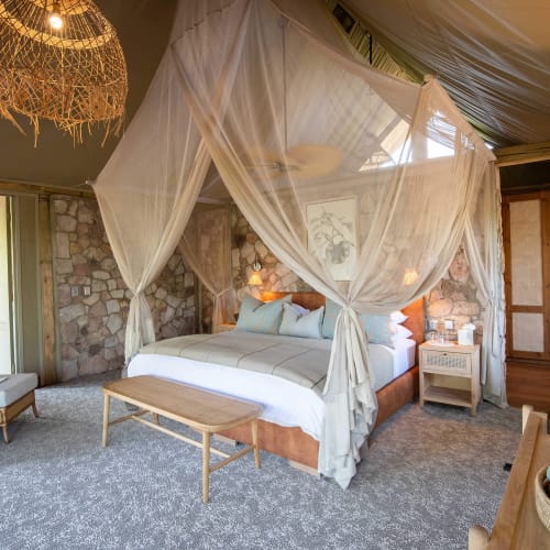 Luxuriöses Schlafzimmer mit einem Baldachinbett, das in dünnen Vorhängen gehüllt ist, Steinwände und Holzmöbel in einem tropischen Ambiente.