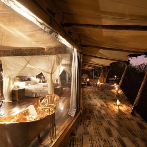 A luxurious guest suite with a viewing deck extending outside, illuminated by small lamps during dusk or night.