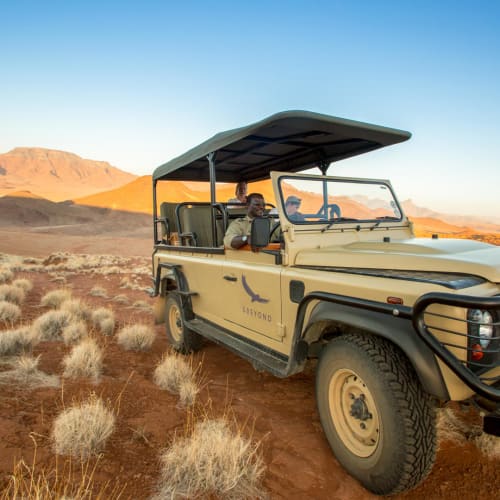 A safari vehicle parked in the desert with mountains in the background at sunset