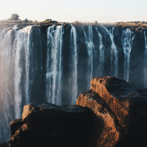Lebendige Ansicht des Viktoriafalls mit herabstürzendem Wasser von einer hohen Klippe, umgeben von Felsen im Vordergrund.