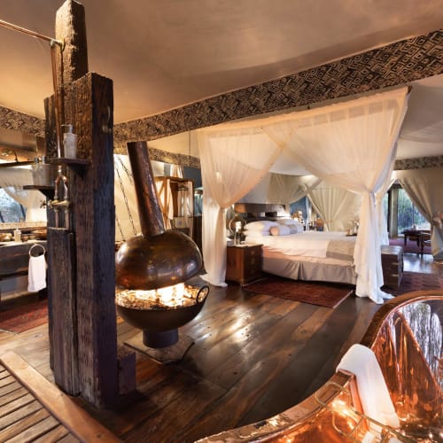 Luxurious guest suite with four-poster bed and rustic decor in a Botswana safari camp.