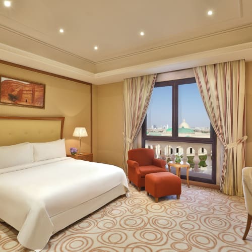Luxurious hotel room with a large bed, two bedside lamps, and a sitting area near a window with curtains.