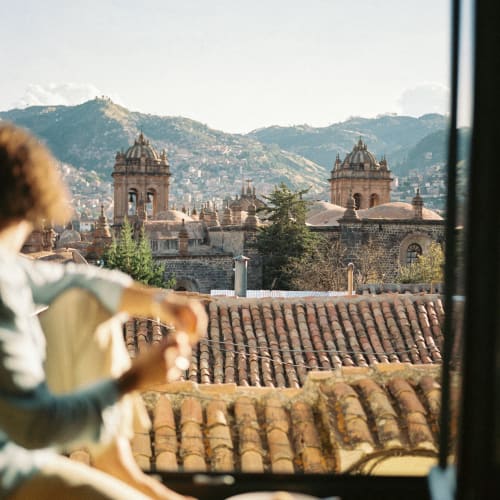 Eine Person sitzt bei einem Fenster und frühstückt mit Blick auf historische Kirchentürme und die Hügel der Stadt im Hintergrund.