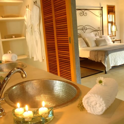 Luxurious bathroom with lit candles and neatly rolled towels leading into a cozy bedroom with a large bed and wooden accents.