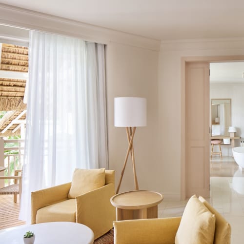 Elegant living room with yellow armchairs, a small round table, and a balcony with wooden furniture and greenery outside.