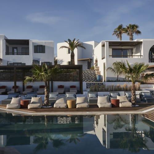 Luxuriöse weiße mediterrane Gebäude mit Balkonen und Palmen, die einen einladenden Swimmingpool mit gepolsterten Sitzgelegenheiten auf dem Deck am Tag umgeben.