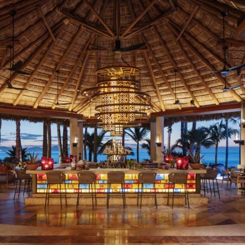 Luxurious open-air bar with tropical decor and a view of the ocean at sunset.