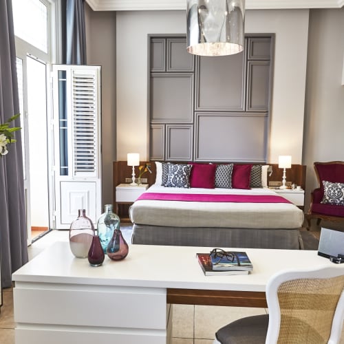 Luxushotelzimmer mit ordentlich gemachtem Bett, Nachtscheinwerfern und eleganter Dekoration, einschließlich Stuhl und Dekorvasen.