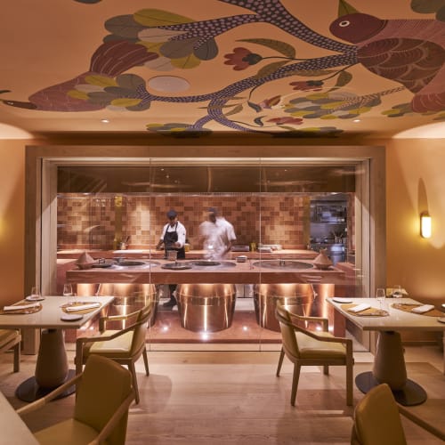 Elegant restaurant interior with a view into the open kitchen, featuring a colorful ceiling mural.