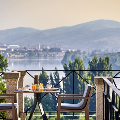 Ein Frühstücksset mit zwei Stühlen und einem kleinen Tisch auf einem Balkon mit Blick auf Weinberge und den Douro-Fluss in Portugal.