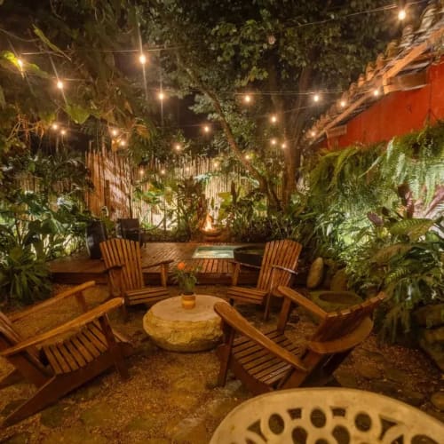 Gemütlicher Außen-Loungebereich bei Nacht mit Lichterketten, Holzstühlen und üppigen grünen Pflanzen.