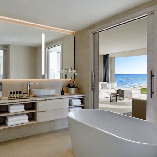 Modern bathroom with a free-standing bathtub overlooking an ocean view through large glass doors.