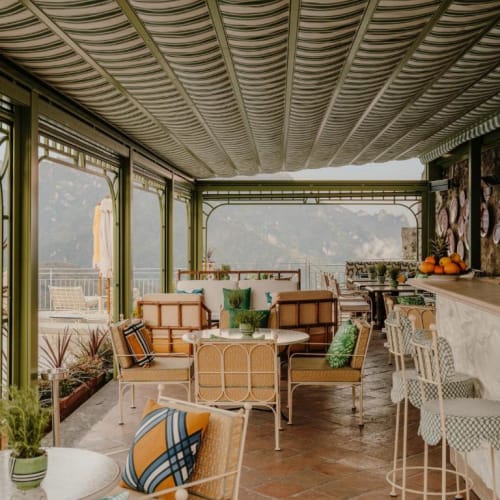 Ein eleganter Innenbereich mit Bar, bequemen Sitzgelegenheiten, grünen Pflanzen und großen Fenstern mit Blick auf eine malerische Küstenlandschaft.