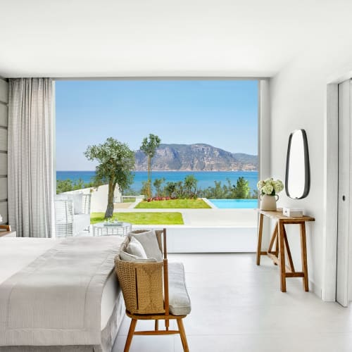 Bright, modern bedroom with large sliding glass doors opening to a view of the pool, garden, and ocean.