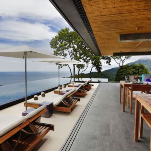 Luxury outdoor terrace with lounge chairs, umbrellas, and dining area overlooking the ocean and lush greenery in Uvita, Costa Rica.